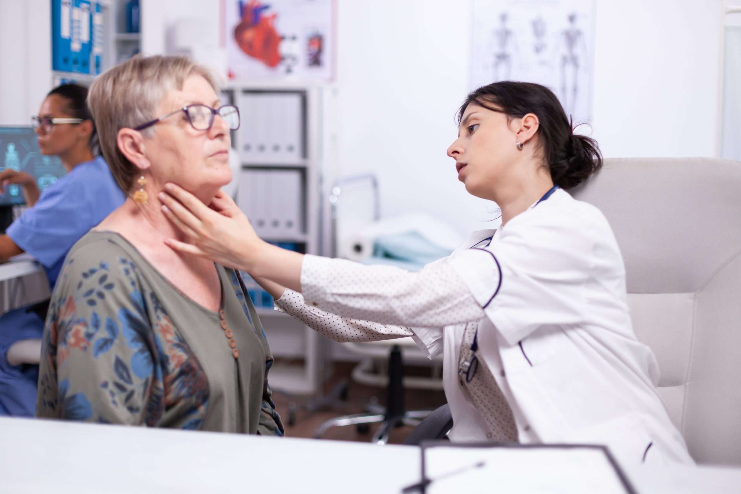 Young medic palpating neck of senior woman