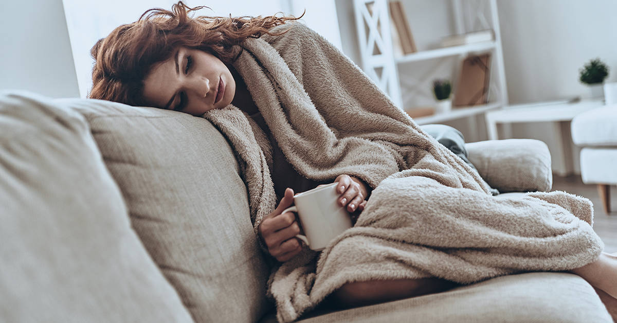 Feeling sick. Sick young women covered with blanket resting at home while sitting on the sofa