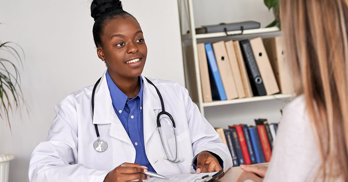 African doctor physician consulting caucasian woman patient at medical visit.