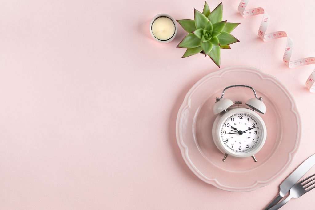 Cutlery with measuring tape and alarm clock on color background.