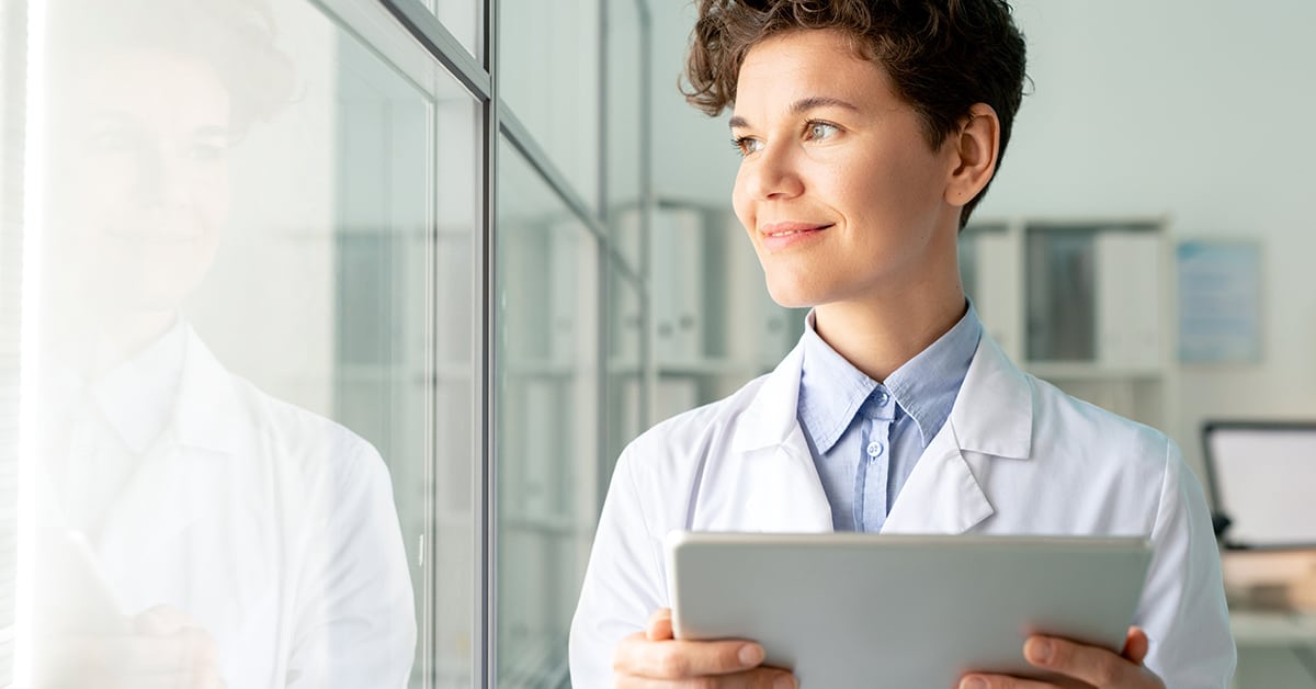 Smiling attractive laboratory worker with curly hair satisfied with research results using digital tablet