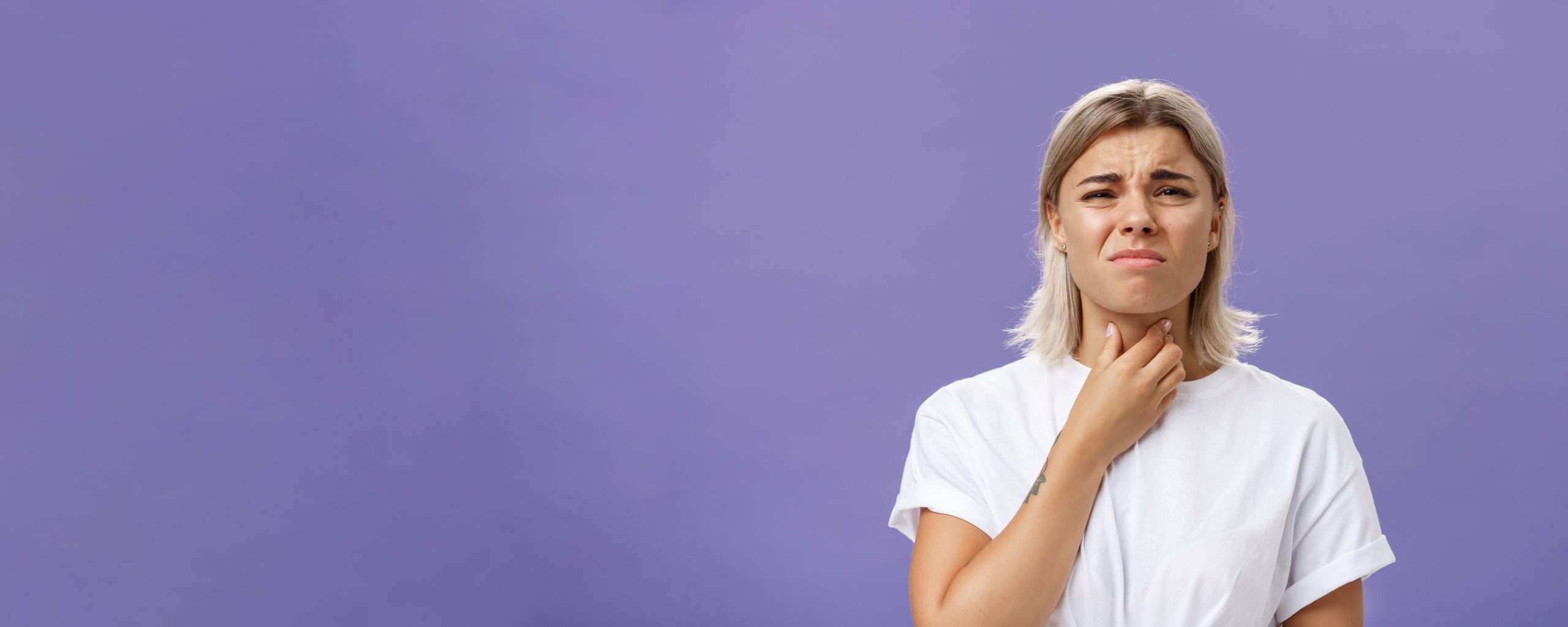 Young woman looks displeased as she feels her throat with her hand