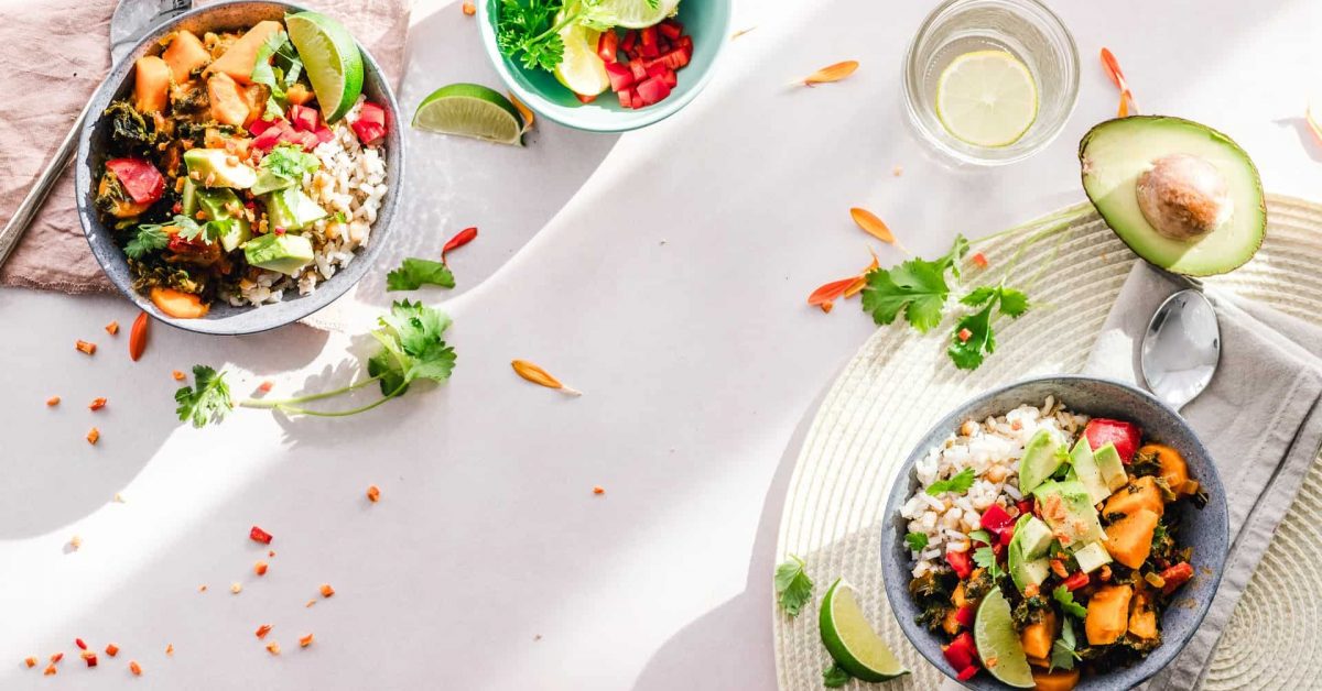 Two bowls of fresh salad with avocado and lime, accompanied by a bowl of fruit, set on a light tablecloth.