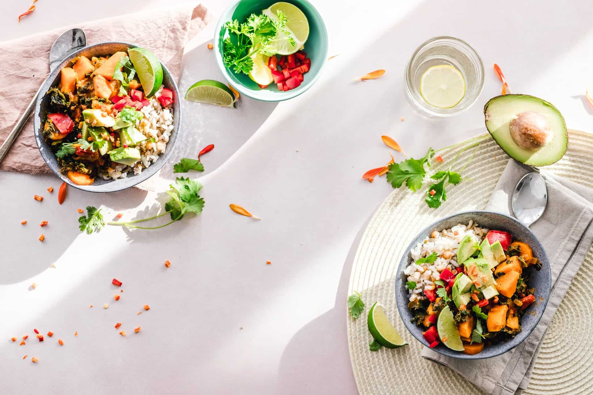 Two bowls of fresh salad with avocado and lime, accompanied by a bowl of fruit, set on a light tablecloth.