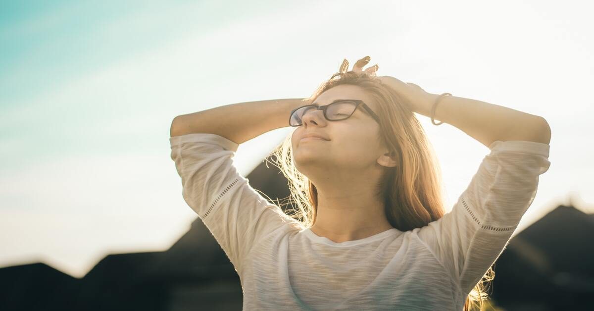 A person stands with their hands on their head, facing a bright sky.