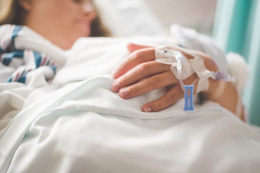 The patient is lying with a catheter in her arm.