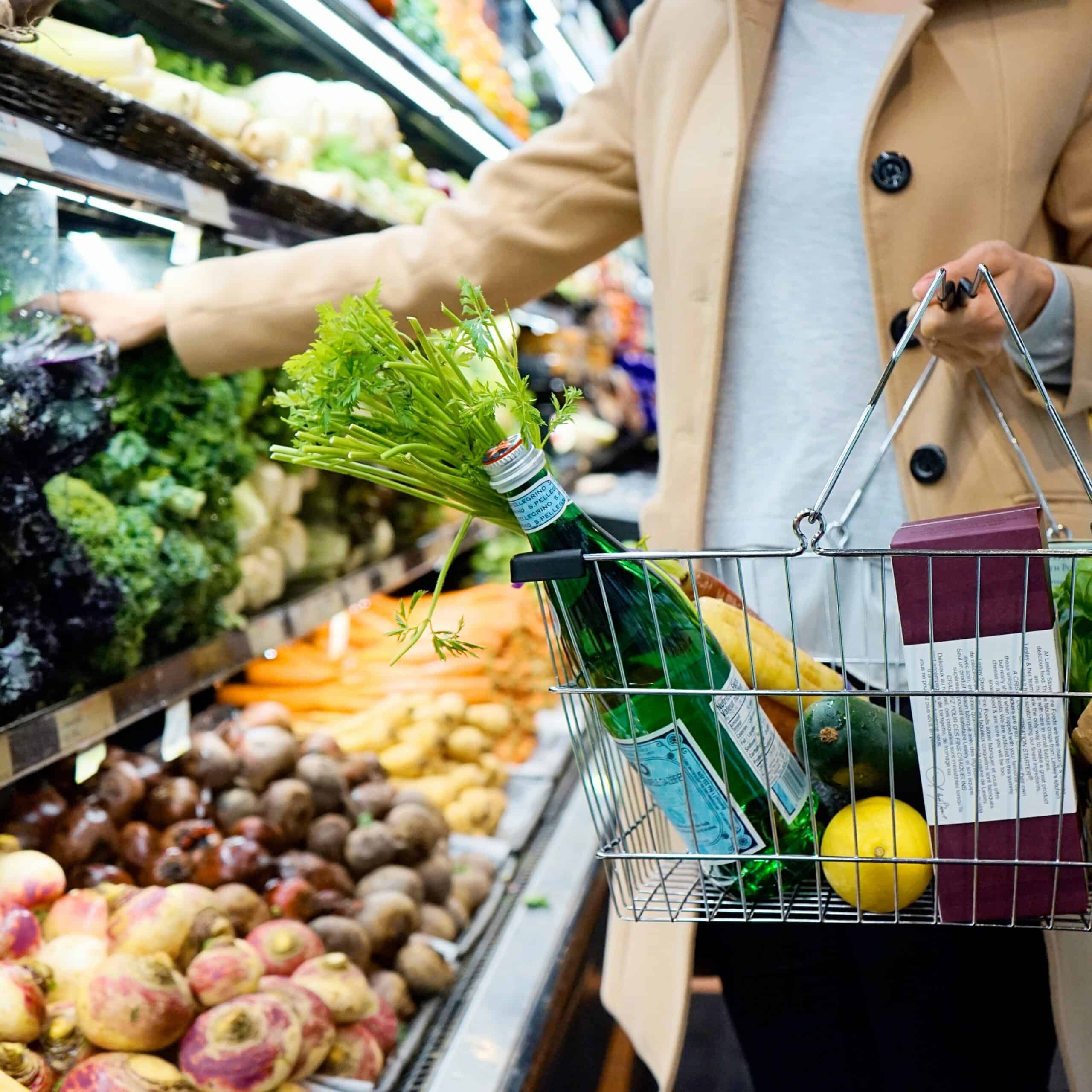 A person with a grocery basket chooses vegetables in the refrigerator