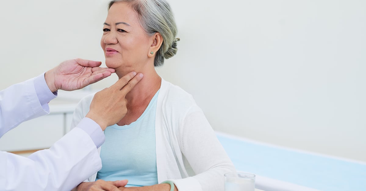 Doctor checking thyroid gland of elderly Vietnamese woman